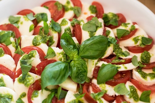 Frische Caprese mit Tomaten, Mozzarella, Basilikum und grünem Pesto auf einem weißen Teller – mediterrane italienische Spezialität mit frischen Zutaten.