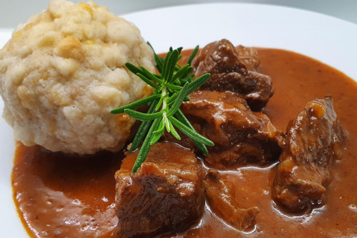 Hausgemachtes Rindsgulasch mit Semmelknödel auf einem weißen Teller – traditionelle österreichische Hausmannskost mit kräftiger Sauce und frischen Kräutern.